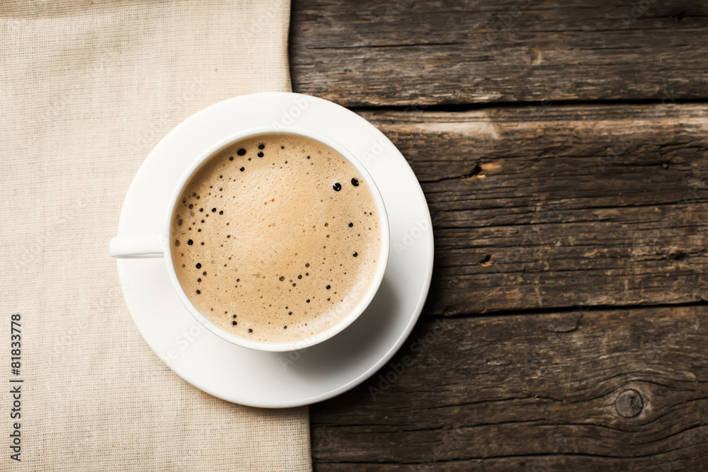 Close-up of coffee cup with roasted coffee beans on wooden background.