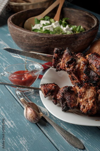 Shashlik with salad on the wooden table.