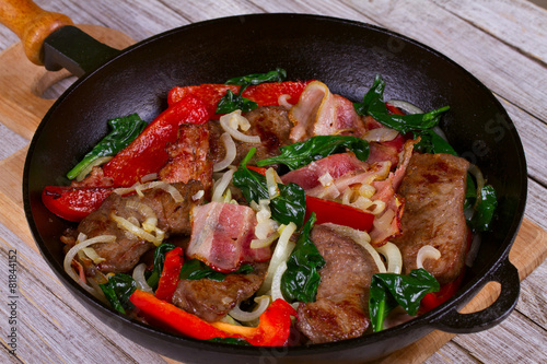 Frying pan with fried meat, bacon, red pepper and spinach
