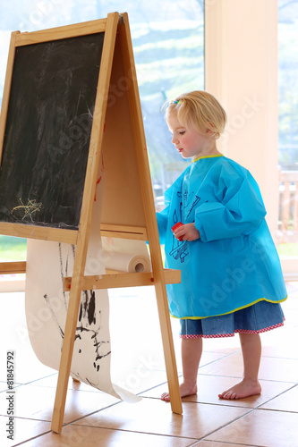 Cute preschooler girl drawing or painting indoors