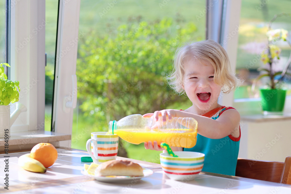 Happy toddler girl enjoying healthy breakfast in sunny kitchen Happy toddler girl enjoying healthy breakfast in sunny kitchen