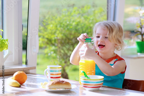 Happy toddler girl enjoying healthy breakfast in sunny kitchen
