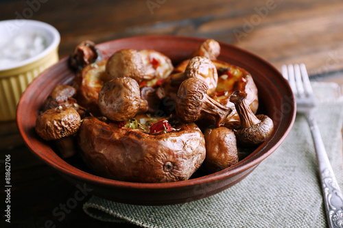 Baked potatoes with mushrooms in bowl and sauce on table close up