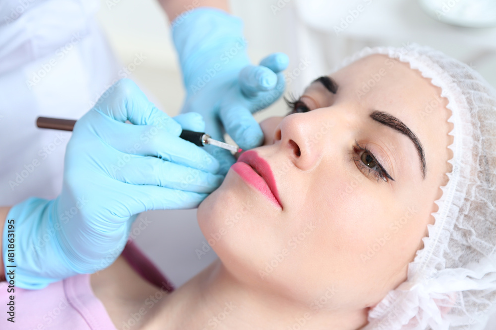 Cosmetologist applying permanent make up on lips Cosmetologist applying permanent make up on lips