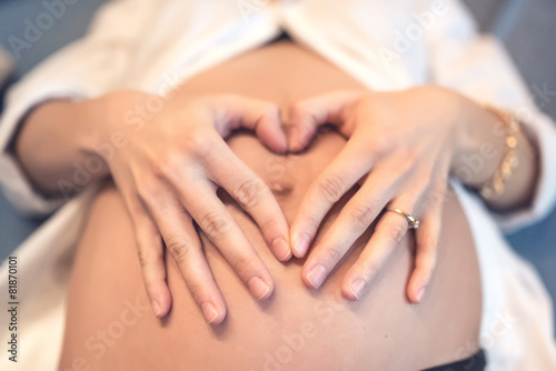 Pregnant young woman holding fingers in a heart shape, tounching