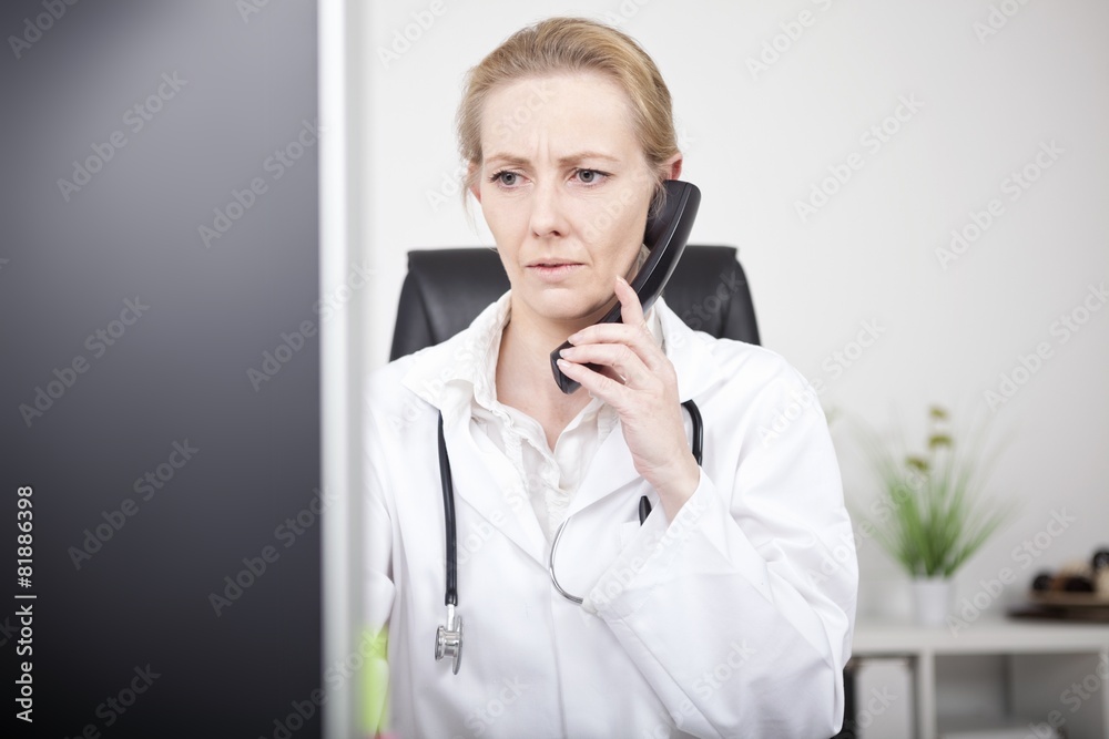 Serious Female Doctor on Phone Looking at Monitor Serious Female Doctor on Phone Looking at Monitor