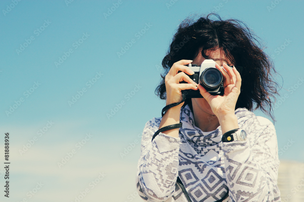 Woman with vintage retro camera having fun on the beach on blue