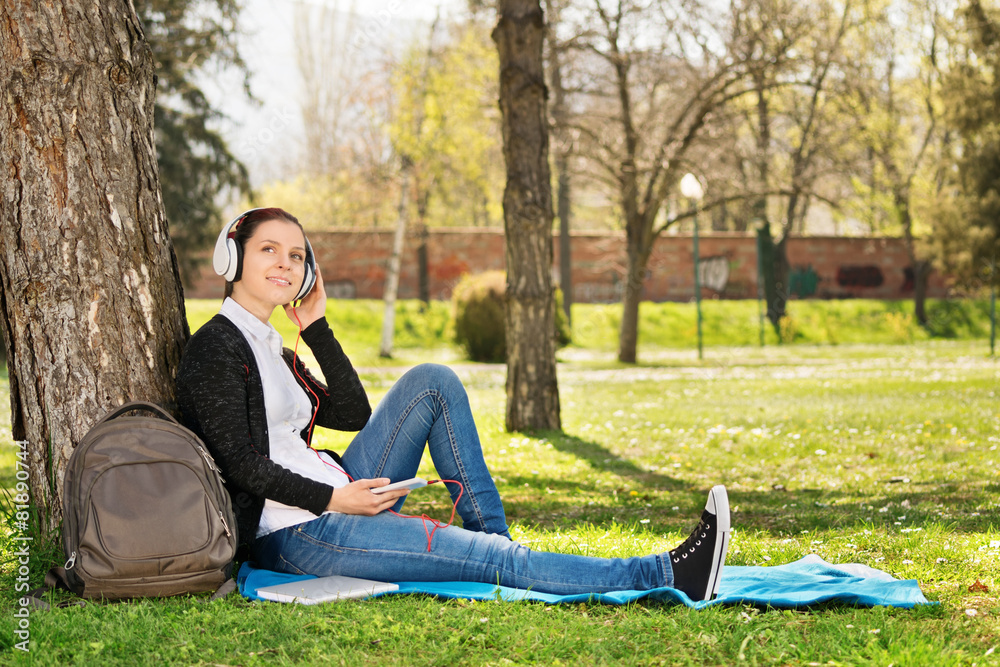 Young girl bent against a tree listening music