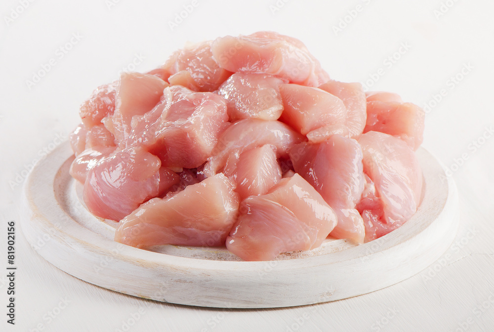 Raw chicken meat on  white wooden cutting board.