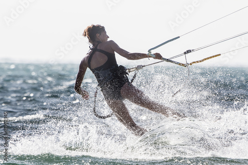 A young woman kite-surfer rides against the sun