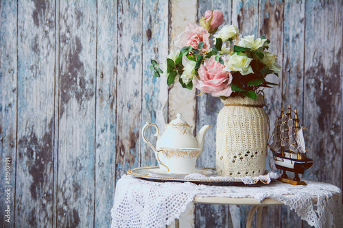 Porcelain teapot and cup on a table with a vase with artificial