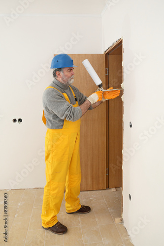 Worker installing wooden door, using polyurethane foam