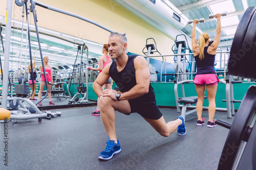 Man stretching and women doing dumbbells exercises in gym