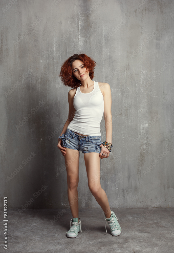 girl in a vest and sneakers standing on a gray background textur