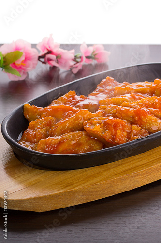 Sweet and sour chicken on a stone plate over wooden background
