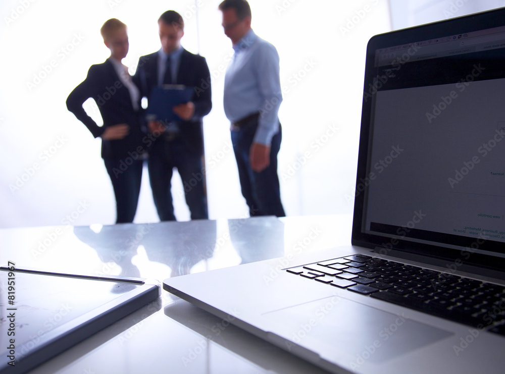 Laptop computer on desk , two businesspeople standing in the Laptop computer on desk , two businesspeople standing in the