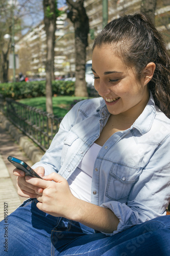 Young beautiful woman using her phone and smiling sitting on a b