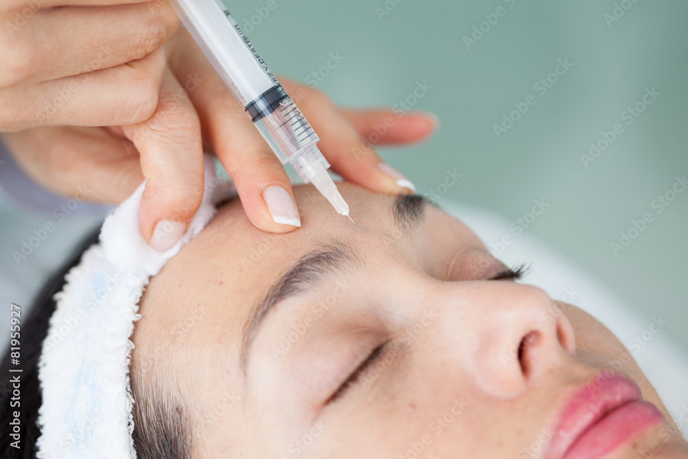Doctora aplicando un tratamiento facial utilizando una jeringa a una paciente joven - obrazy, fototapety, plakaty 
