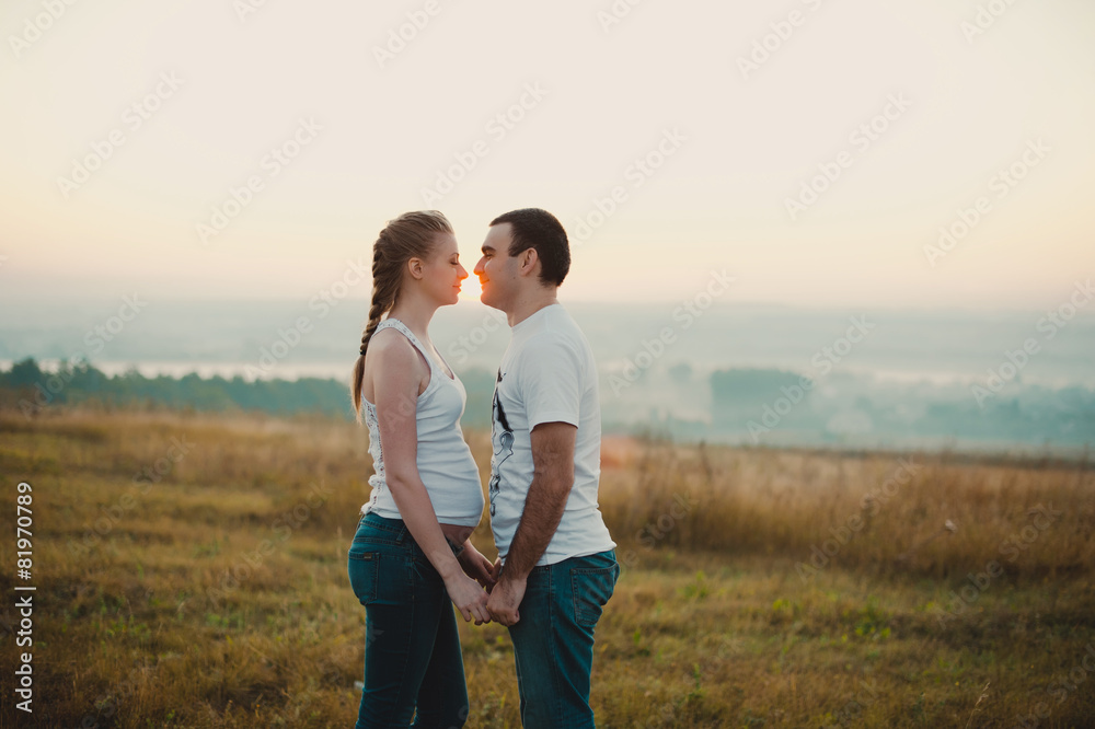 Young pregnant couple holding hands and standing in a field Young pregnant couple holding hands and standing in a field