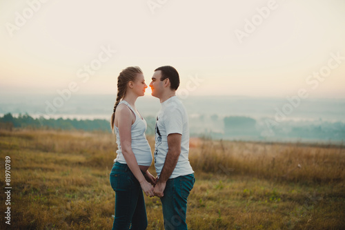 Young pregnant couple holding hands and standing in a field 