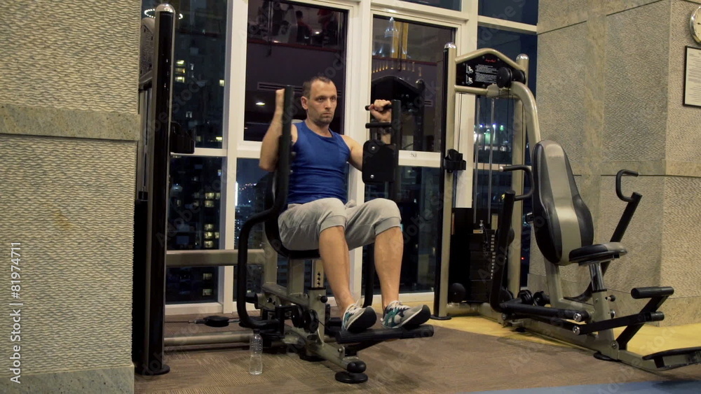Young man exercising on machine in gym at night Young man exercising on machine in gym at night