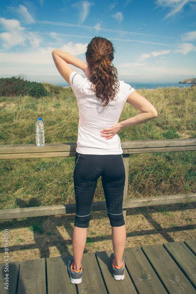 Athletic woman touching neck and back muscles by injury Athletic woman touching neck and back muscles by injury