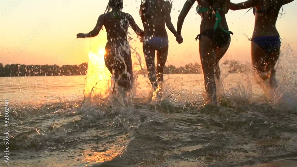 Group of happy girls running and playing in water at the beach