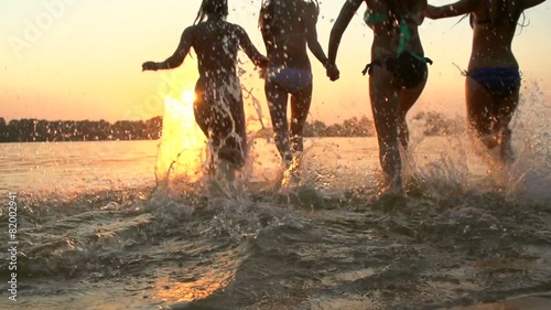 Group of happy girls running and playing in water at the beach