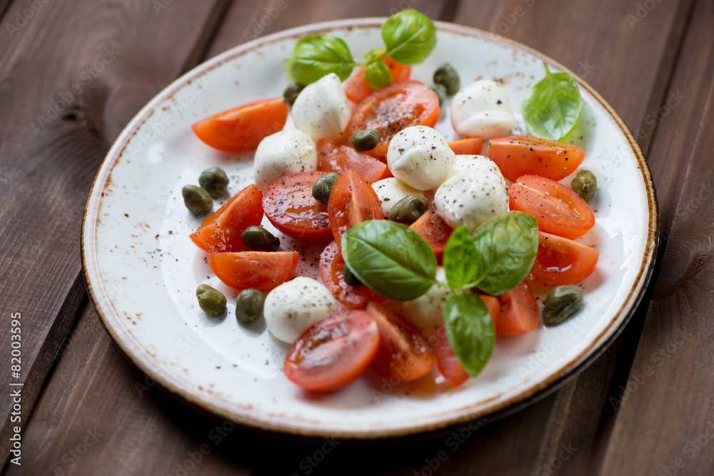 Caprese salad with capers on a glass plate, studio shot
