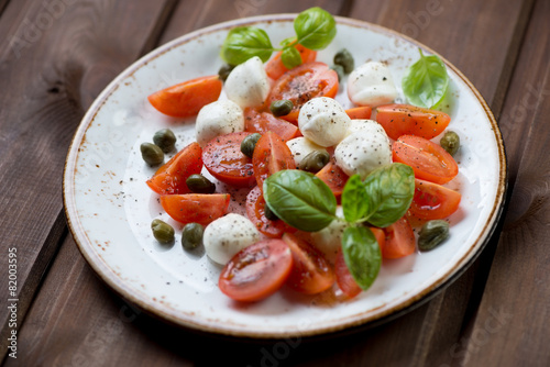 Caprese salad with capers on a glass plate, studio shot