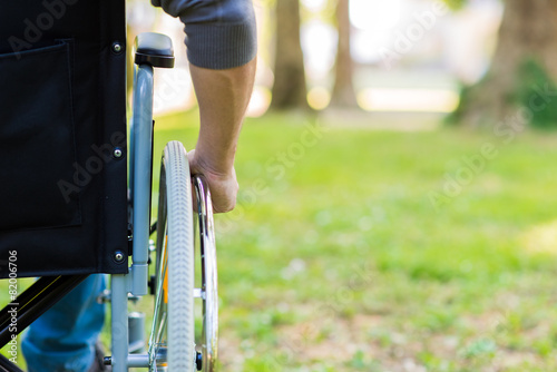Male hand on wheel of wheelchair during walk in park photo