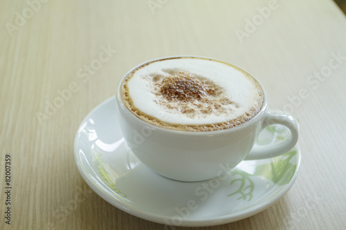 A cup of coffee with heart pattern in a white cup on wooden back