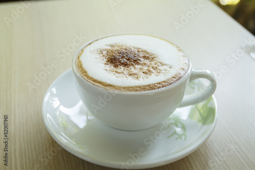 A cup of coffee with heart pattern in a white cup on wooden back