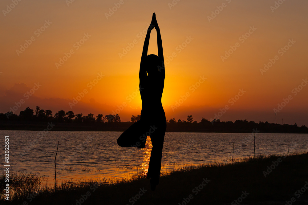Silhouette young woman practicing yoga at orange sunset.