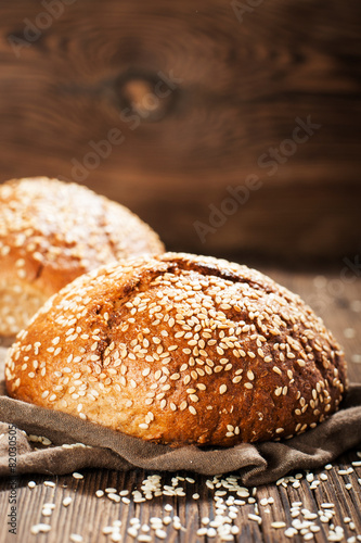 Fresh rye buns with sesame seeds on a wooden background
