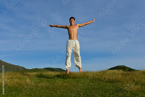 Young Man jumping on a green meadow with blue sky    