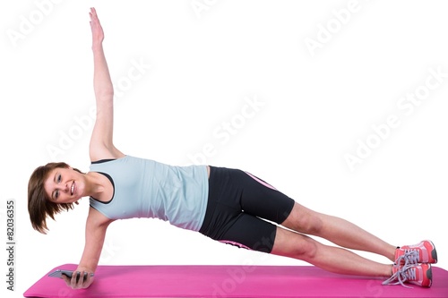 brunette looking at camera and doing side plank on exercise mat