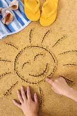 Smiling sun happy smiley face drawing drawn in sand with child hands on a tropical beach with seashells and accessories summer holiday vacation photo vertical