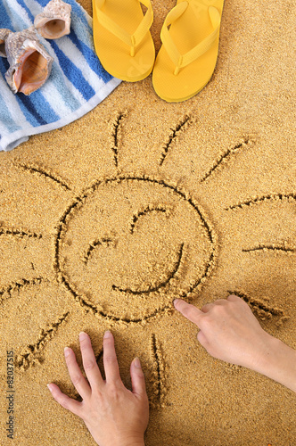 Smiling sun happy smiley face drawing drawn in sand with child hands on a tropical beach with seashells and accessories summer holiday vacation photo vertical