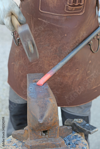skilful blacksmith takes the hot iron with a hammer on the anvil