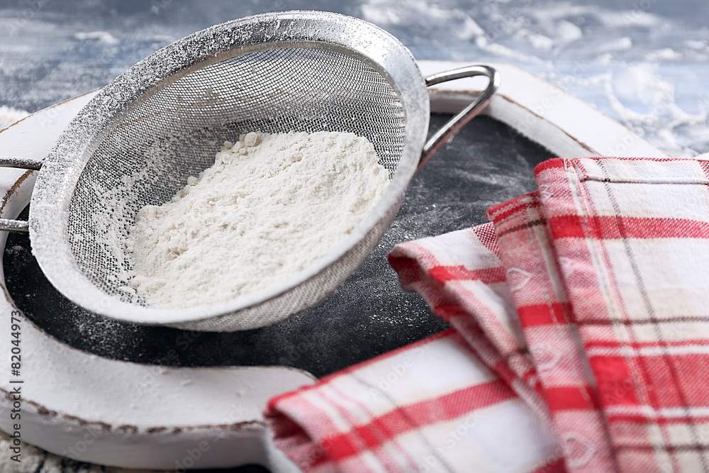 Fototapeta premium Sifting flour through sieve on wooden table, closeup
