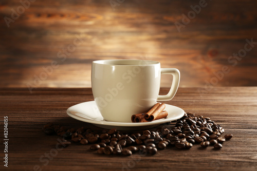 Cup of coffee with grains and cinnamon sticks on wooden background