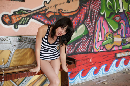 brunette in striped top near the broken piano in an abandoned ro