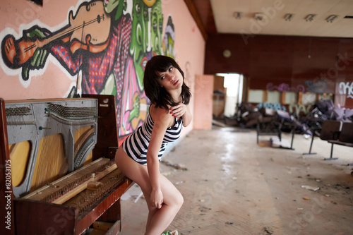 brunette in striped top near the broken piano in an abandoned ro