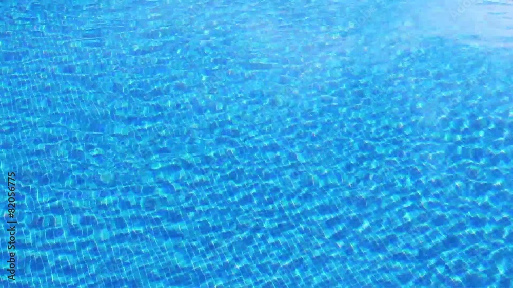 Waving clear water in swimming pool with blue bottom, top view.