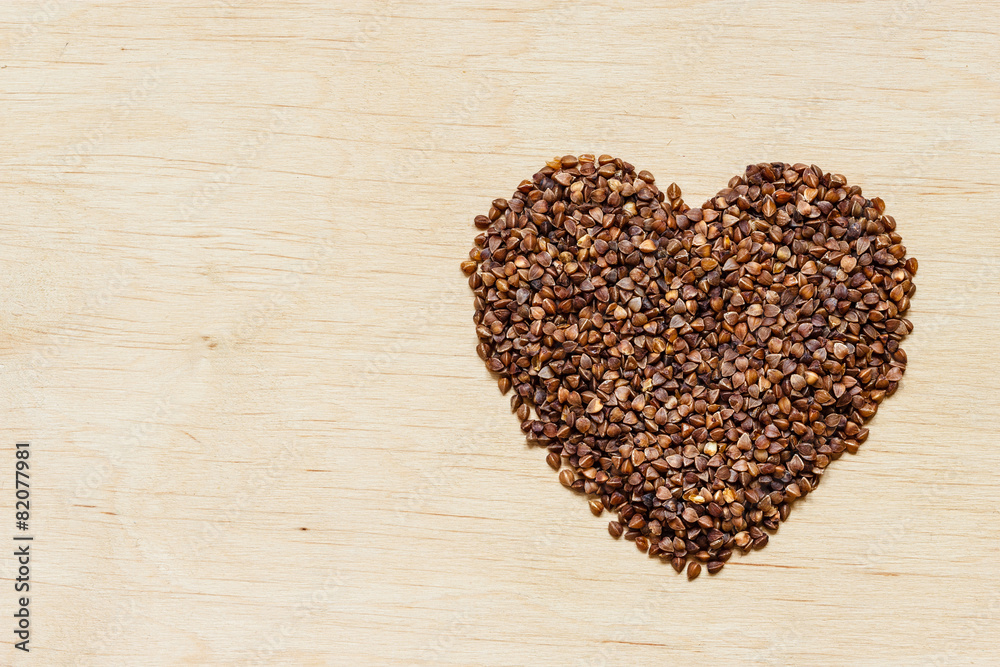 buckwheat groats heart shaped on wooden surface.