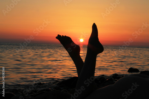 Naked woman legs and evening beach on the sunset