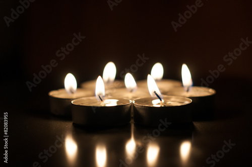Several candles on a dark background reflected from the surface