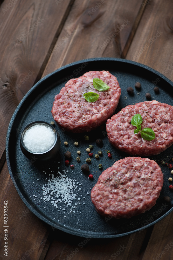 Frying pan with raw beef cutlets over wooden background Frying pan with raw beef cutlets over wooden background