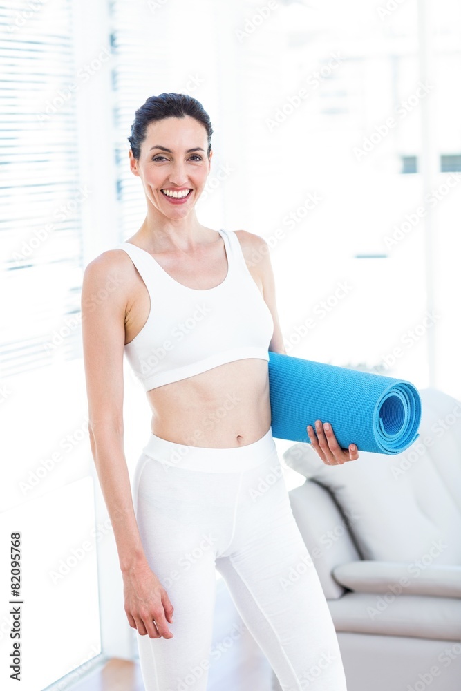 Smiling brunette holding exercise mat